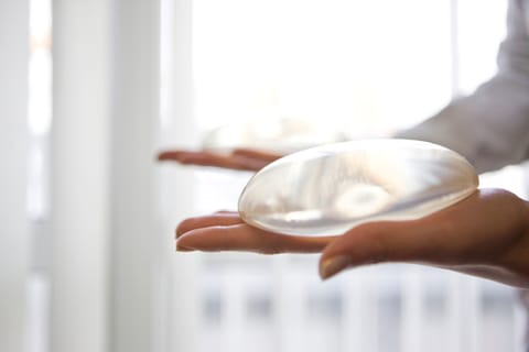 Ein rundes Silikon-Brustimplantat in einer behandschuhten Hand vor hellem Hintergrund