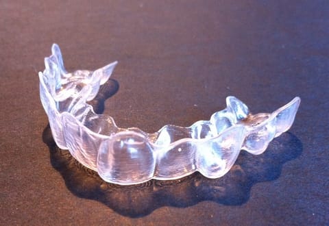 A clear removable orthodontic aligner tray resting on a dark surface